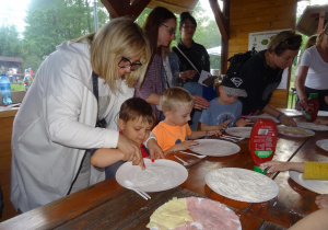 Dzieci przygotowują pizzę z pomocą rodziców.
